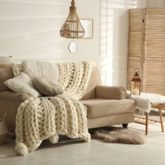 Cozy living room interior with beige sofa, knitted blanket and cushions